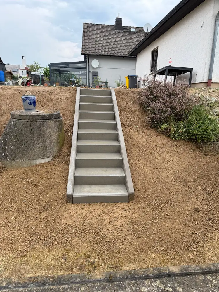 Neue Treppe aus grauen Blockstufen mit Randeinfassung in einem Erdhang vor einem Wohnhaus