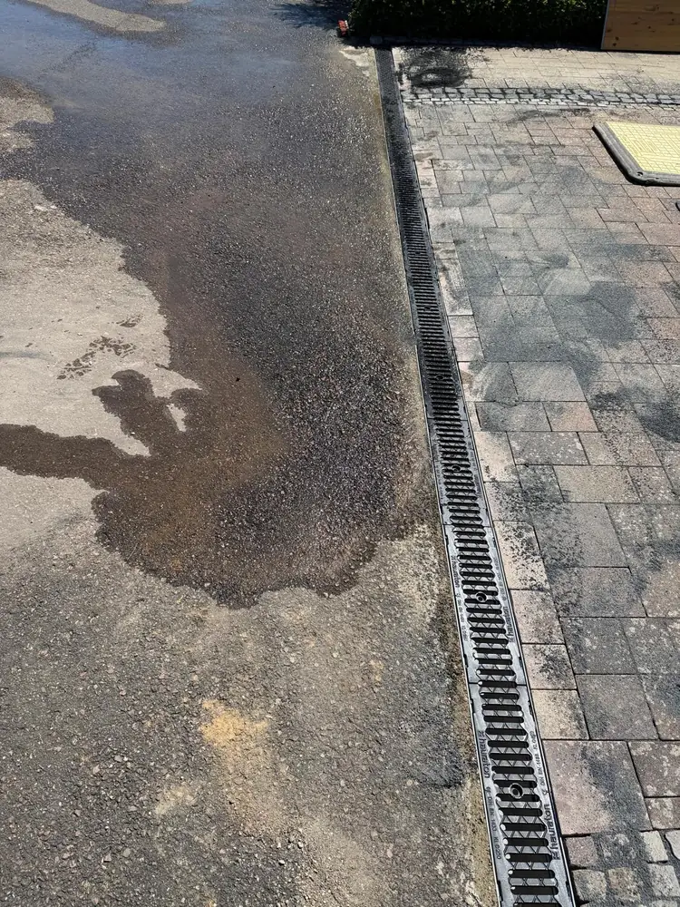 Neu gesetzte Entwässerungsrinne mit Gussrost zwischen Asphaltfläche und Pflaster
