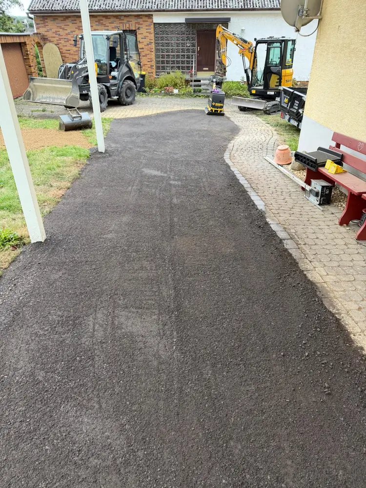 Verdichteter Gehweg aus Schotter 0/16 neben einem Pflasterweg, im Hintergrund Radlader, Minibagger und Rüttelplatte