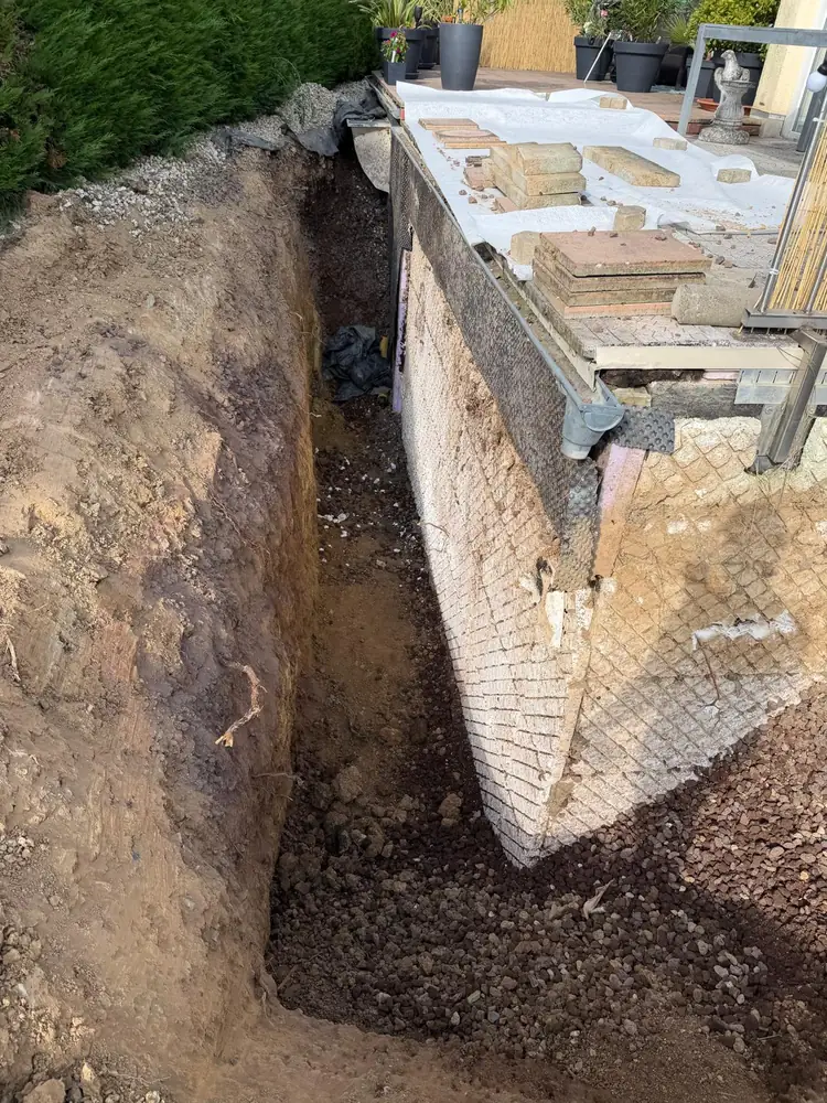 Freigelegte Kelleraußenwand in einem ausgehobenen Graben neben einer Terrasse
