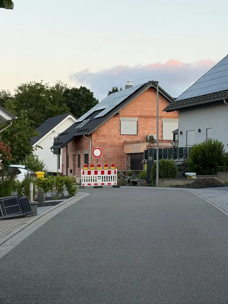 Straßensperrung mit rot-weißer Absperrschranke, Warnleuchten und Verkehrsschild in einem Wohngebiet